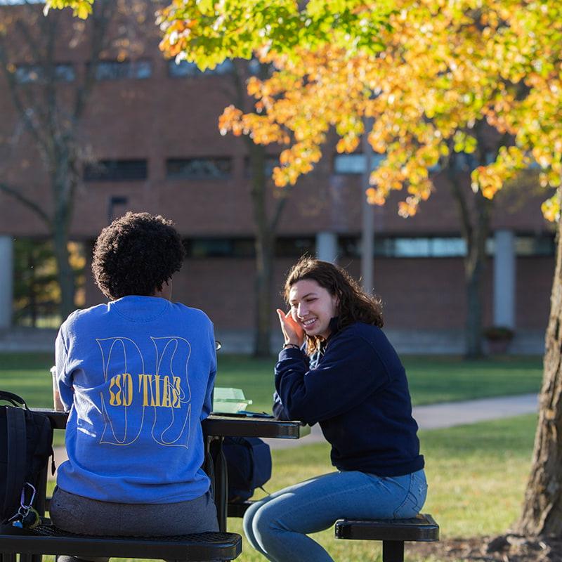 Two Drake University students sitting on a bench outside on campus talking
